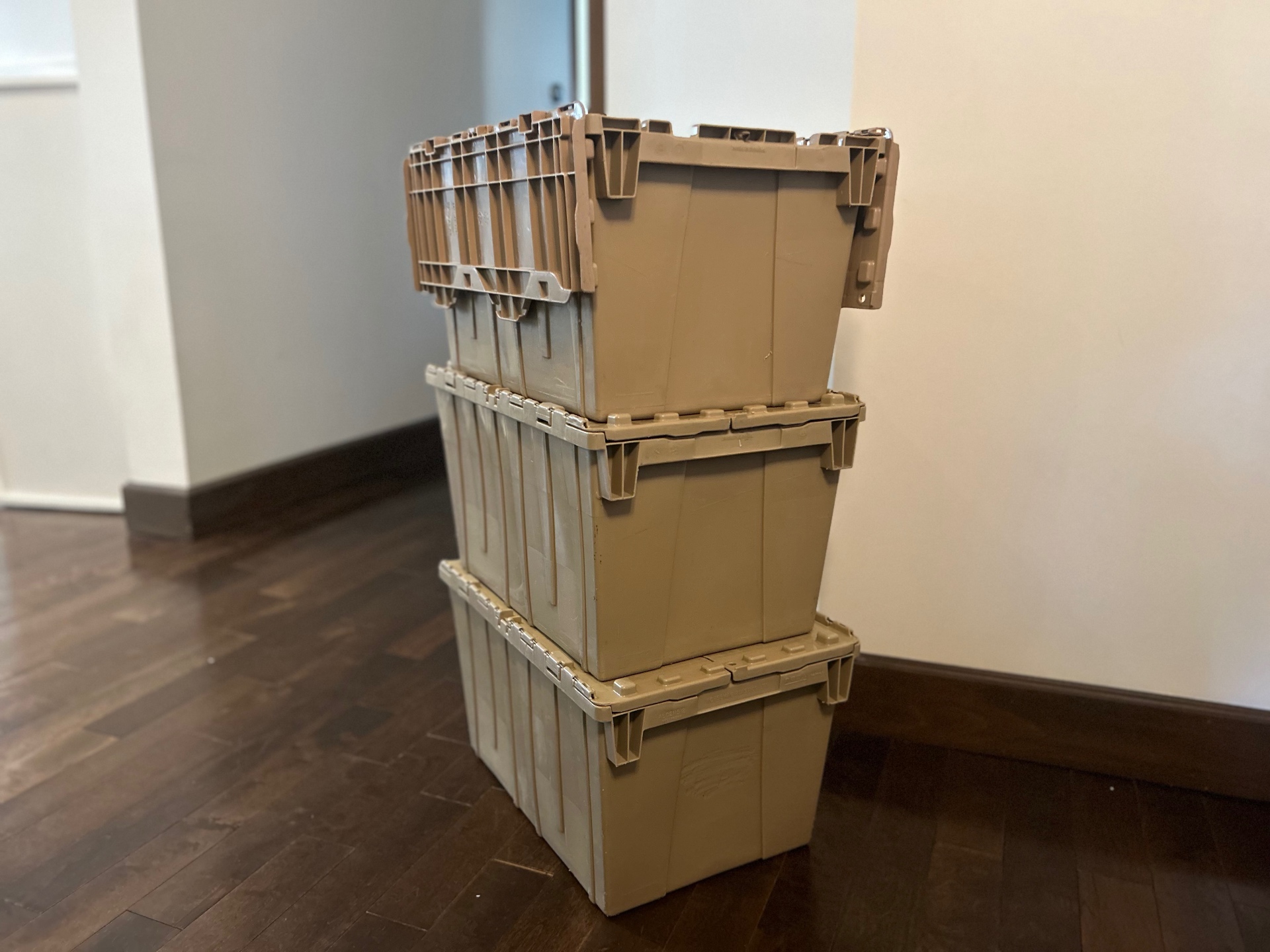 Three stacked tan moving bins with attached lids inside a home